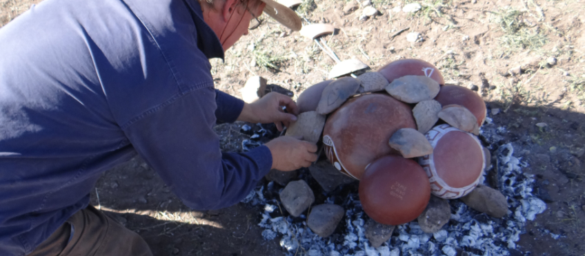 Placing cover sherds on an open fired pottery firing 