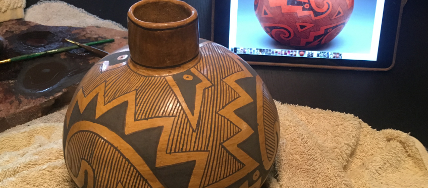 Replica Anasazi pottery being carefully painted using a photo of the original.